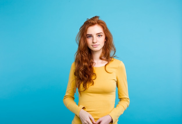 Portrait of young beautiful ginger woman with tender serious face crossing arms looking at camera. Isolated on pastel blue background. Copy space.