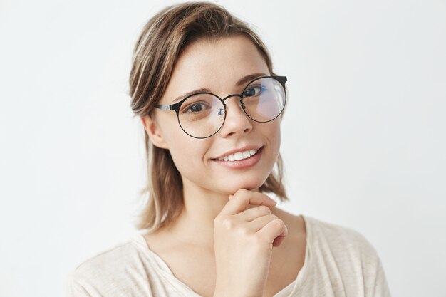 Portrait of young beautiful girl in glasses smiling holding hand on chin .