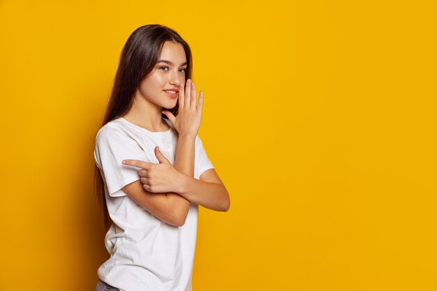 Portrait of young beautiful girl posing isolated over yellow studio background Whispering