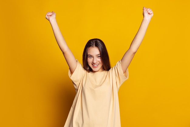 Portrait of young beautiful girl posing isolated over yellow studio background Winning