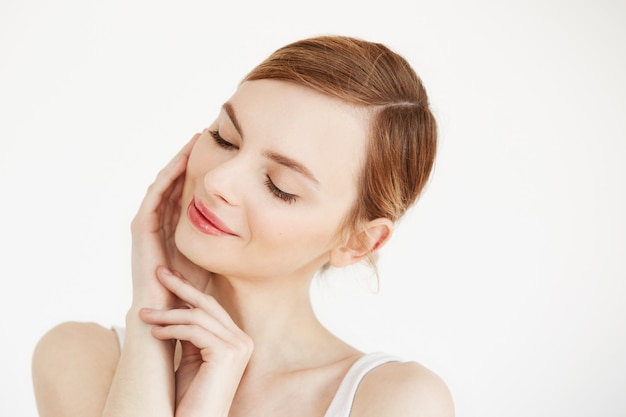 Portrait of young beautiful girl smiling with closed eyes touching face . Facial treatment. Beauty cosmetology and skincare.