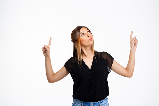 Portrait of young beautiful girl over white background. Copy space. point up