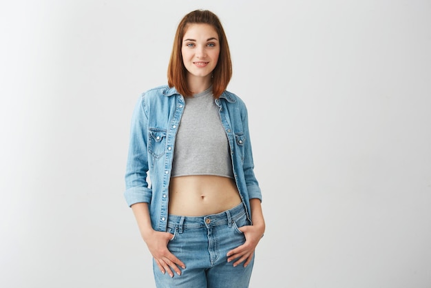 Portrait of young beautiful happy girl in jean jacket smiling looking at camera over white wall