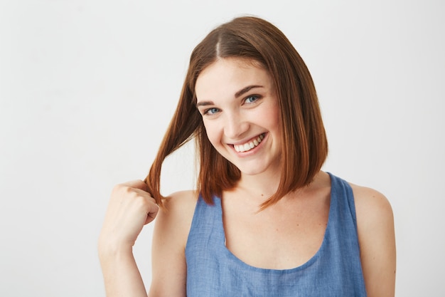 Portrait of young beautiful happy girl with natural make up smiling touching hair .