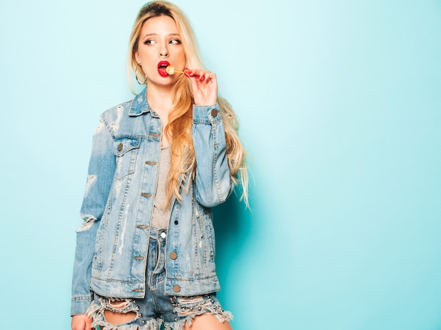 Portrait of young beautiful hipster bad girl in trendy jeans  clothes and earring in her nose.  Positive model licking round sugar candy
