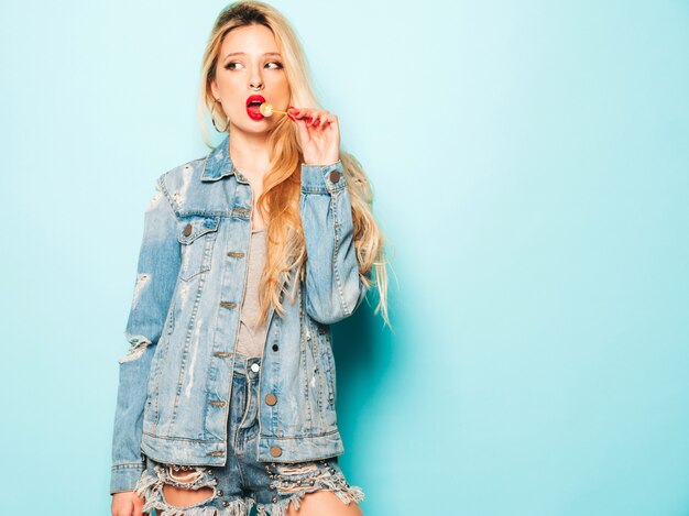 Portrait of young beautiful hipster bad girl in trendy jeans  clothes and earring in her nose.  Positive model licking round sugar candy