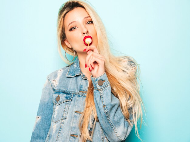 Portrait of young beautiful hipster bad girl in trendy jeans  clothes and earring in her nose.  Positive model licking round sugar candy