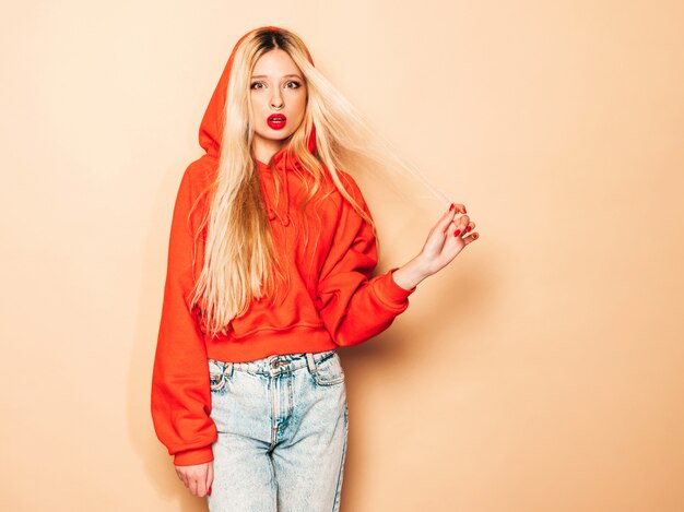 Portrait of young beautiful hipster bad girl in trendy red  hoodie and earring in her nose.Sexy carefree blond woman posing in studio.Positive model having fun