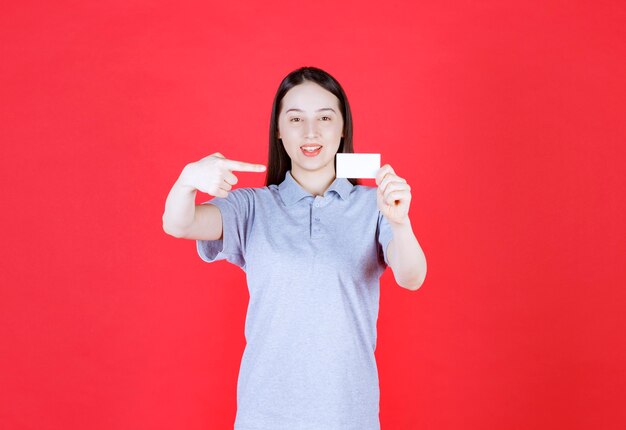 Portrait of young beautiful lady holding visit card and point finger on it