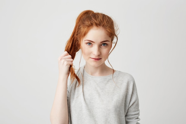 Ritratto di giovane bella ragazza rossa toccando la coda dei capelli.