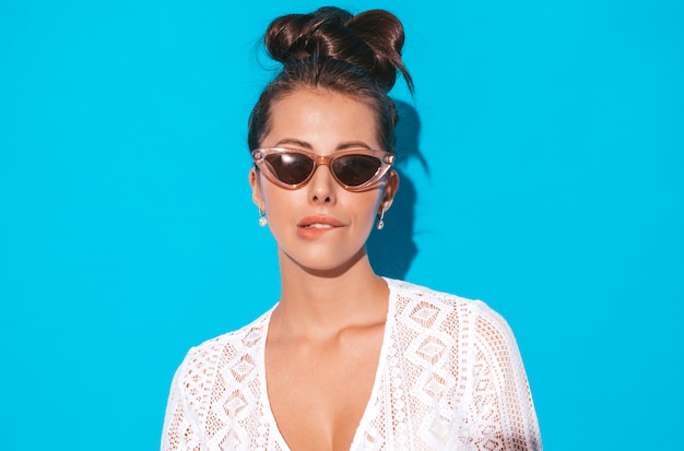 Free photo portrait of young beautiful sexy smiling woman with ghoul hairstyle. trendy girl in casual summer white hipster suit clothes in sunglasses. hot model isolated on blue.biting her lip