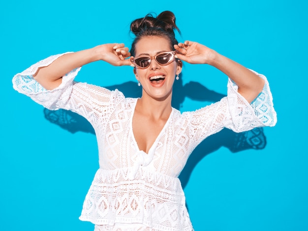 Portrait of young beautiful sexy smiling woman with ghoul hairstyle. Trendy girl in casual summer white hipster suit clothes in sunglasses. Hot model isolated on blue