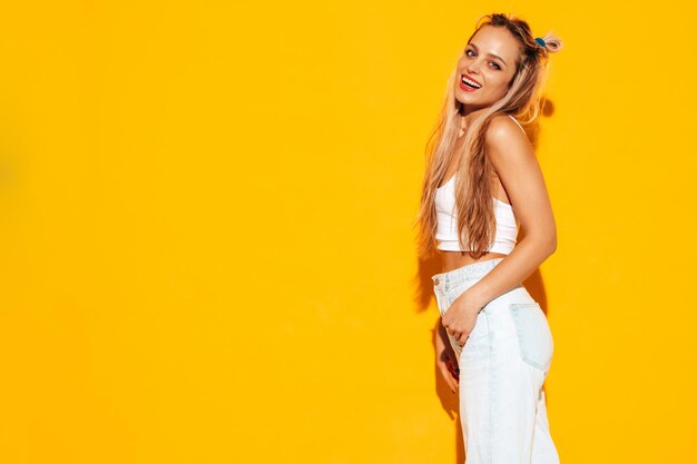 Portrait of young beautiful smiling blond female in trendy summer clothes Sexy carefree woman posing near yellow wall in studio Positive model having fun indoors Cheerful and happy