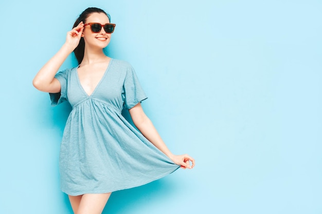 Portrait of young beautiful smiling female in trendy summer blue dress Sexy carefree woman posing near blue wall in studio Positive model having fun and going crazy Cheerful and happy