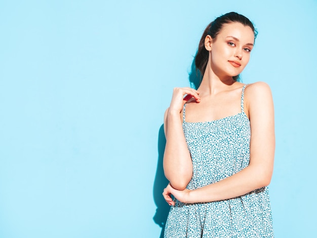 Portrait of young beautiful smiling female in trendy summer blue dress Sexy carefree woman posing near blue wall in studio Positive model having fun and going crazy Cheerful and happy