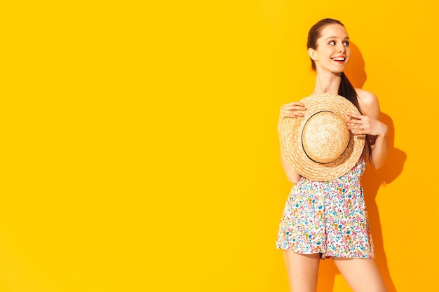 스튜디오의 노란색 벽 근처에서 포즈를 취한 근심 없는 여성의 트렌디한 여름 드레스를 입은 젊은 아름다운 미소의 초상화 실내에서 즐거운 시간을 보내는 긍정적인 모델
