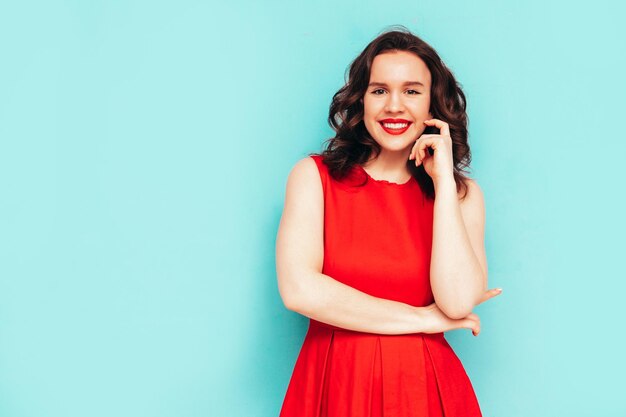 Portrait of young beautiful smiling female in trendy summer dress Sexy carefree woman posing near blue wall in studio Positive model having fun and going crazy Cheerful and happy