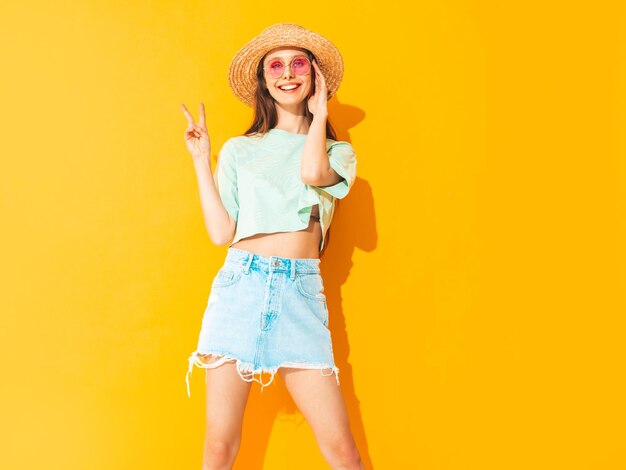 Portrait of young beautiful smiling female in trendy summer jeans skirt carefree woman posing near yellow wall in studio Positive model having fun indoors Cheerful and happy In hat