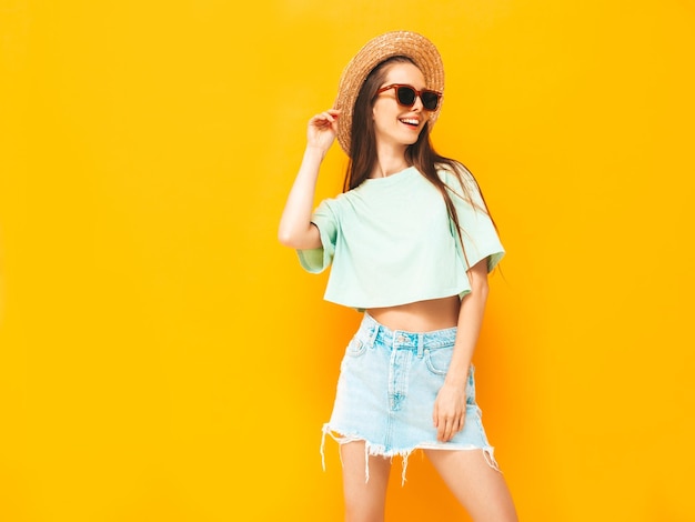 Ritratto di giovane bella donna sorridente in jeans estivi alla moda gonna donna spensierata in posa vicino al muro giallo in studio modello positivo divertendosi al chiuso allegro e felice nel cappello