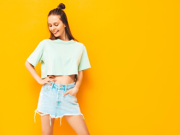 Portrait of young beautiful smiling female in trendy summer jeans skirt carefree woman posing near yellow wall in studio Positive model having fun indoors Cheerful and happy