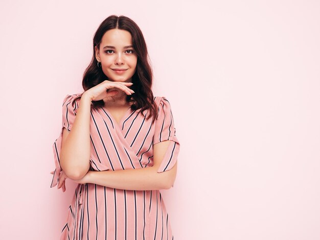 Portrait of young beautiful smiling female in trendy summer pink dress Sexy carefree woman posing near wall in studio Positive model having fun indoors Cheerful and happy