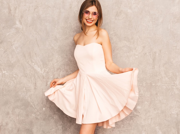 Portrait of young beautiful smiling girl in trendy summer light pink dress. Sexy carefree woman posing. Positive model having fun