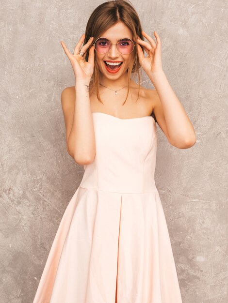 Портрет молодой красивой улыбающейся девушки в модном летнем светло-розовом платье. Сексуальная беззаботная женщина позирует. Позитивная модель с удовольствием