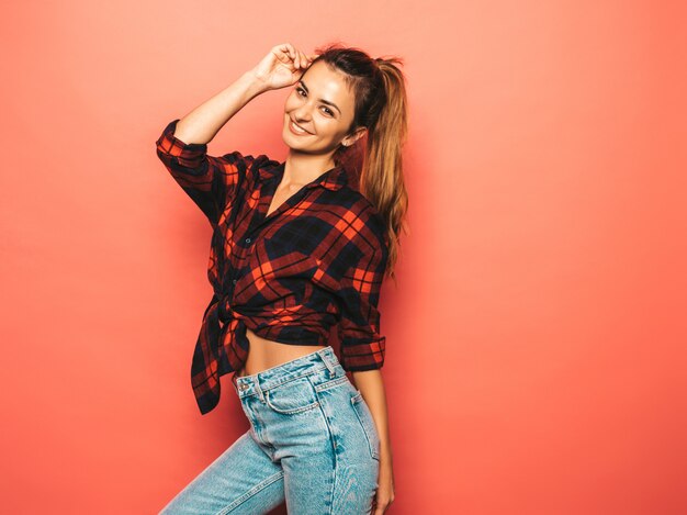최신 유행 여름 체크 무늬 셔츠와 청바지 옷에 젊은 아름 다운 웃는 hipster 여자의 초상화. 스튜디오에서 분홍색 벽 근처 포즈 섹시 평온한 여자. 메이크업이없는 긍정적 인 모델