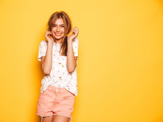 Portrait of young beautiful smiling hipster girl in trendy summer jeans shorts clothes. Sexy carefree woman posing near yellow wall. Positive model having fun