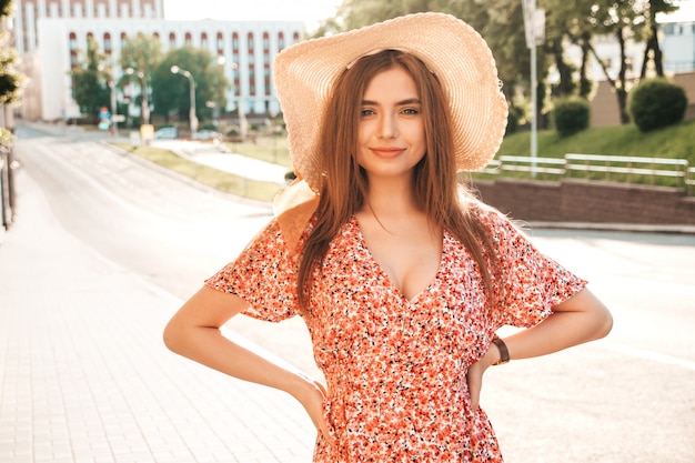 유행 여름 sundress에 젊은 아름 다운 웃는 hipster 여자의 초상화. 일몰에 모자에 거리 배경에 포즈 섹시 평온한 여자. 긍정적 인 모델 야외