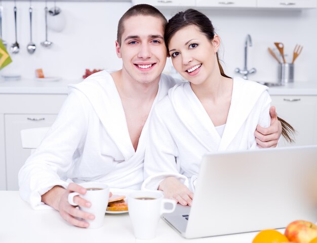 Portrait of young beautiful smiling lovers in the kitchen with laptop