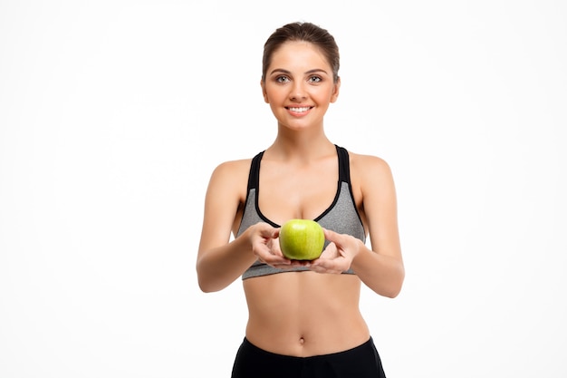 Portrait of young beautiful sportive girl holding apple over white background.