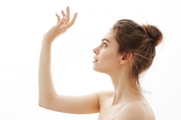 Portrait of young beautiful tender naked woman with bun posing in profile over white background.