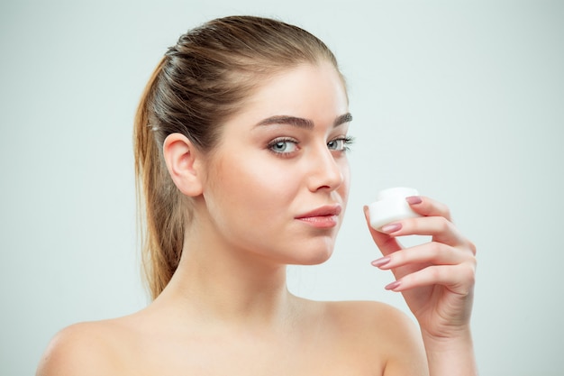 Portrait of young beautiful woman applying moisturizing cream on her face