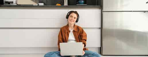 Free photo portrait of young beautiful woman in headphones sits on floor with laptop works from home student