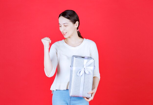 Portrait of young beautiful woman holding gift box and squeezing her fist