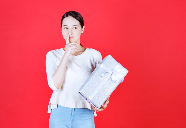 Portrait of young beautiful woman holding gift box and thinking