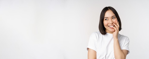 Free photo portrait of young beautiful woman korean girl laughing and smiling looking coquettish standing against white background