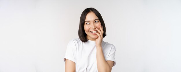 白い背景に立っているコケティッシュな顔をして笑って笑っている若い美しい女性韓国の女の子の肖像画