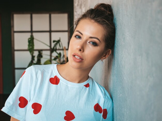 Portrait of young beautiful woman looking at camera  Trendy girl in casual summer white t-shirt  Funny and positive female posing near gray wall in studio