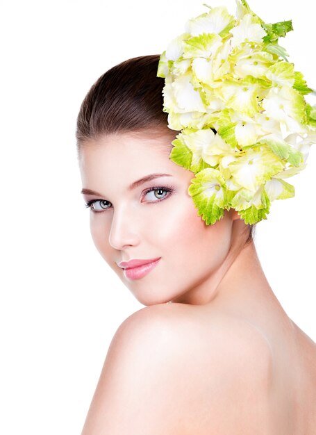 健康できれいな肌を持つ若い美しい女性の肖像画。顔の近くに花を持つきれいな女性-白い背景で隔離。