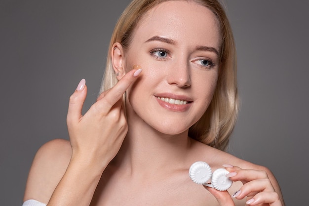 Portrait of young beautiful woman with natural makeup and contact eye lens in hand. Close-up of female model holding white lens box. Eye care and healthy lifestyle. Eyes health.