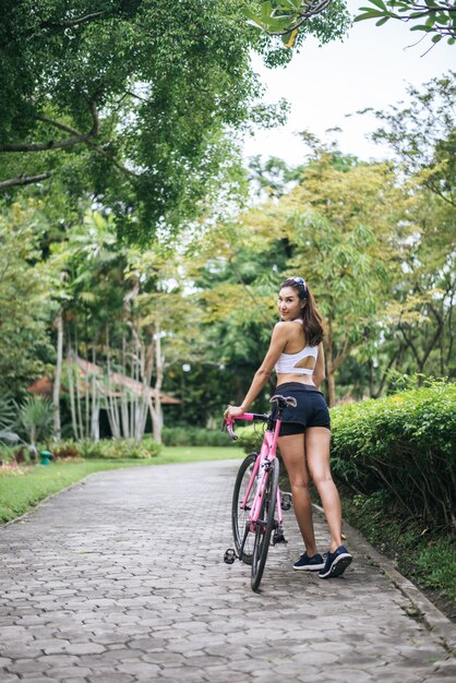 공원에서 분홍색 자전거와 함께 젊은 아름 다운 여자의 초상화. 행동 건강 한 여자.