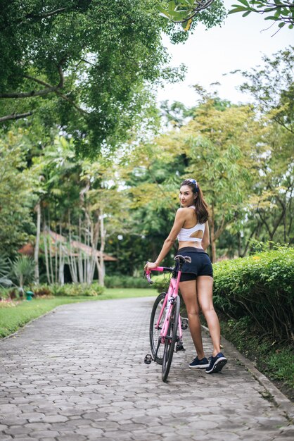 公園でピンクのバイクを持つ若い美しい女性の肖像画。魅力的な健康な女性。