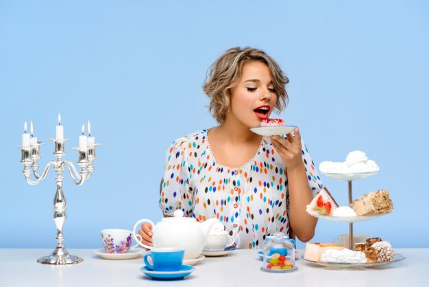 Portrait of young beautiful woman with sweets over blue wall
