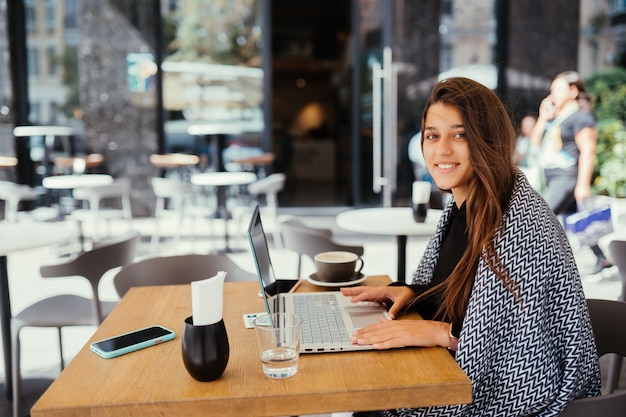 Free photo portrait of a young beautiful women work on portable laptop computer, charming female student using net-book while sitting in cafe