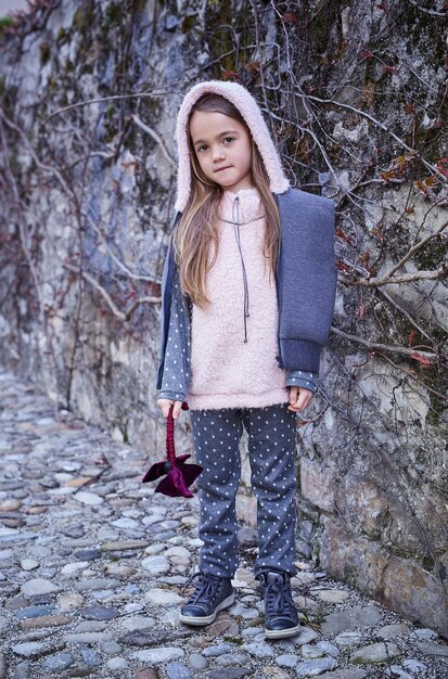自然な灰色の背景の上の暖かい秋の服を着た若いブロンドの女の子の肖像画。