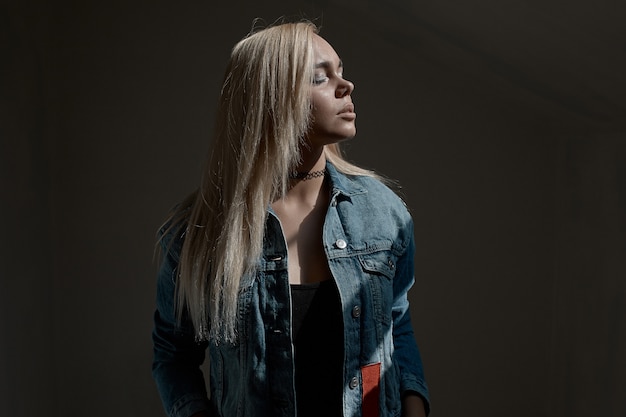 Portrait of young blond woman on dark wall