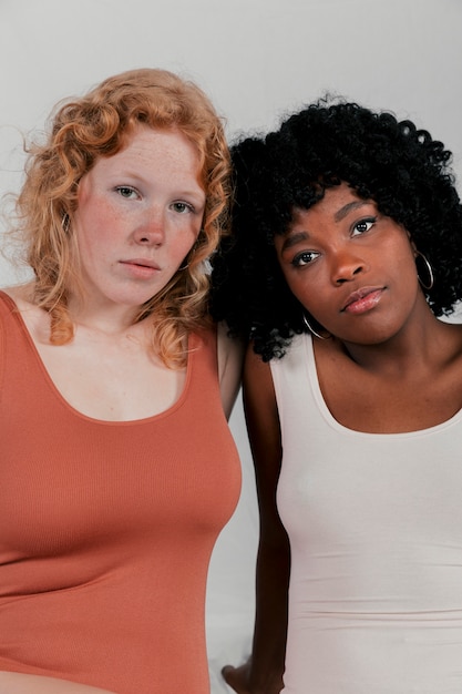 Free photo portrait of young blonde and african women against grey backdrop