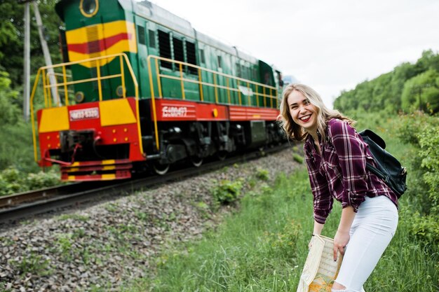 Портрет молодой блондинки в клетчатой рубашке рядом с поездом с картой